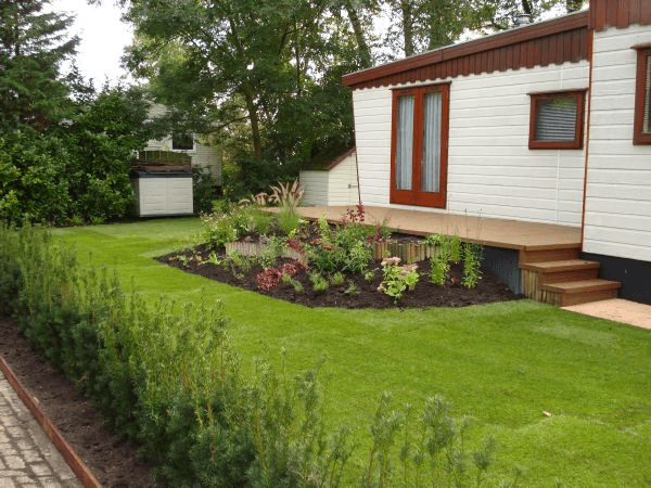 Afgewerkte tuin met vlonder, borders met beplanting en strak gazon.