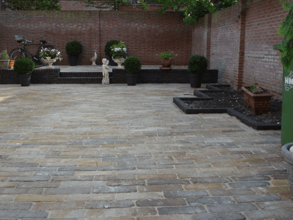 Achtertuin met sierbestrating, rode bakstenen muren en beplanting in bakken.