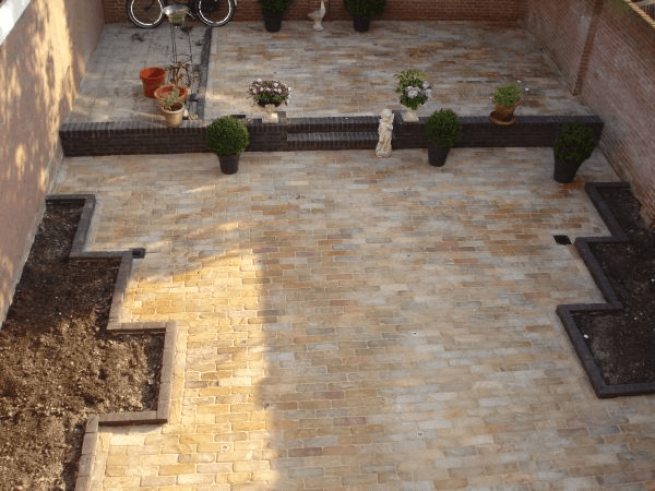 Twee niveaus bestrating met inbouwspots en bakstenen muren.