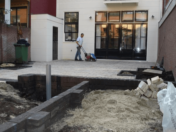 Terras in aanleg met trilplaat en klinkers bij woonhuis.