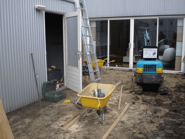 Bouwplaats met minigraver en materiaal tijdens tuinrenovatie.