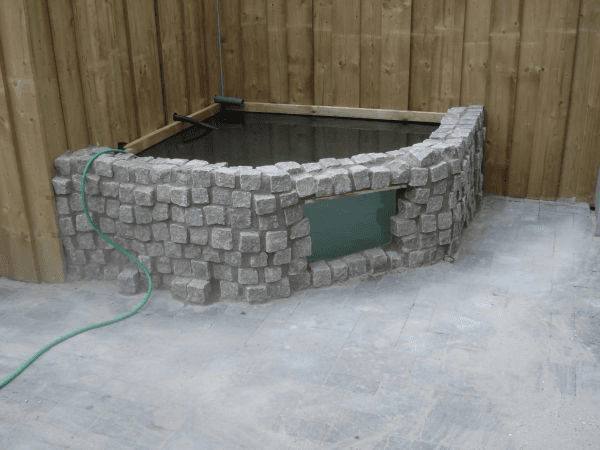 Verhoogde vijver met glazen raam, klinkermetselwerk en houten omlijsting.