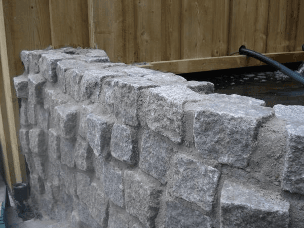 Detail grijze keermuur van kinderkoppen bij waterpartij.