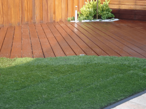 Terrasvlak van groeven hout naast gazon en schutting.