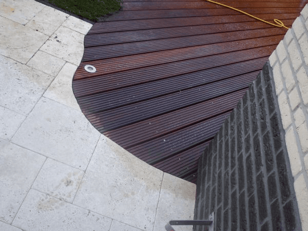 Overgang gebogen houten vlonder, lichte tegels en donkere baksteen.