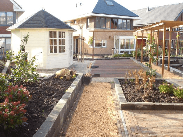 Luxe achtertuin met witte prieel, verhoogde borders, vlonder en pergola bij moderne woning.