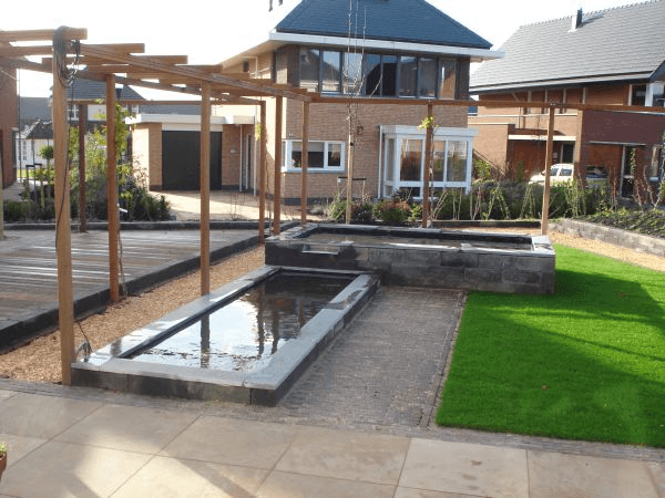 Overzicht tuin met vlonder, vijvers, gazon en bestrating bij nieuwbouwwoningen.