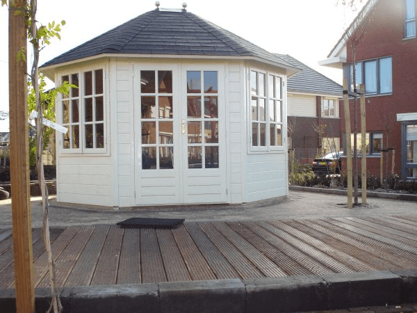 Witte achthoekige tuinkamer met donker dak en vlonder op de voorgrond.