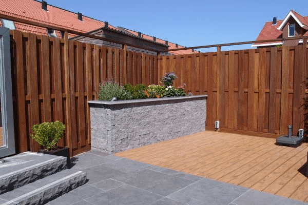 Binnenterras met donkere tegels, houten vlonder en verhoogde plantenbak met bloemen.