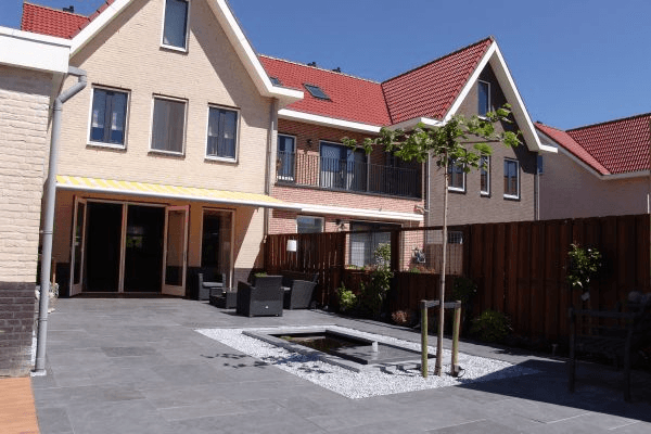 Patio met vijver, loungeset, zonnescherm en openslaande deuren naar de woning.