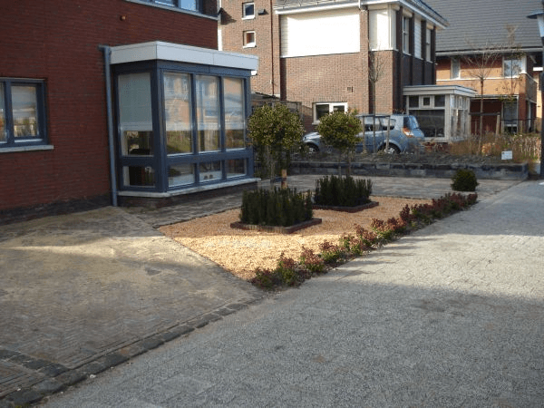 Voortuin bij rode bakstenen woning: klinkers in visgraat, grindbed met strakke beplanting en sierbomen.