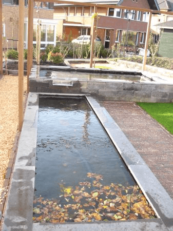 Tweelaags rechthoekig vijversysteem onder houten pergola, met grijze bekleding en klinkerpad naast gazon.